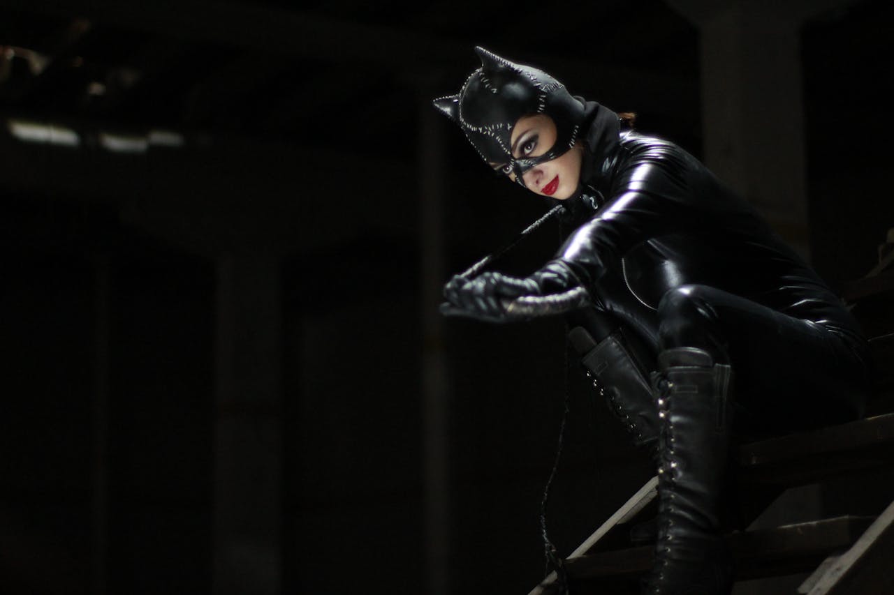 menu-01 A woman in a cat-themed latex suit sits dramatically in an urban setting.